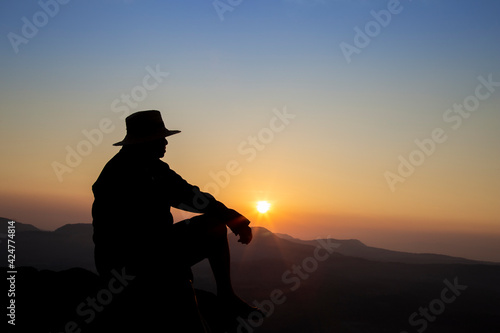 Silhouette of old man sitting on mountain peak during sunrise, man enjoying with nature view, landscape © Pituk