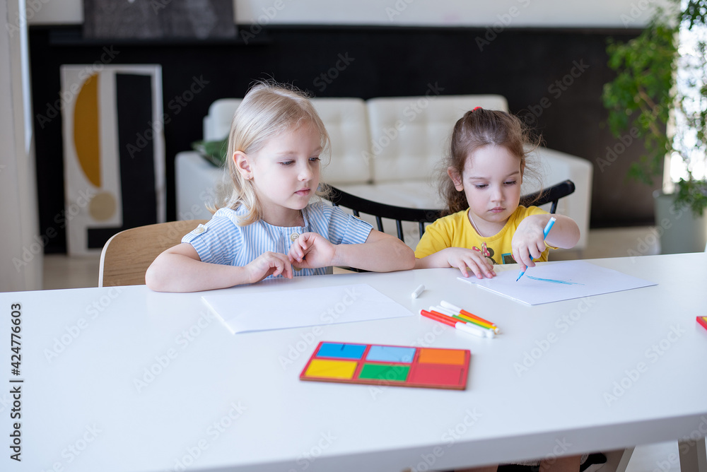 Two girls are engaged in Montessori development classes, at a white table in their room. home learning concept Two girls are engaged in Montessori development classes, at a white table in their room. home learning concept