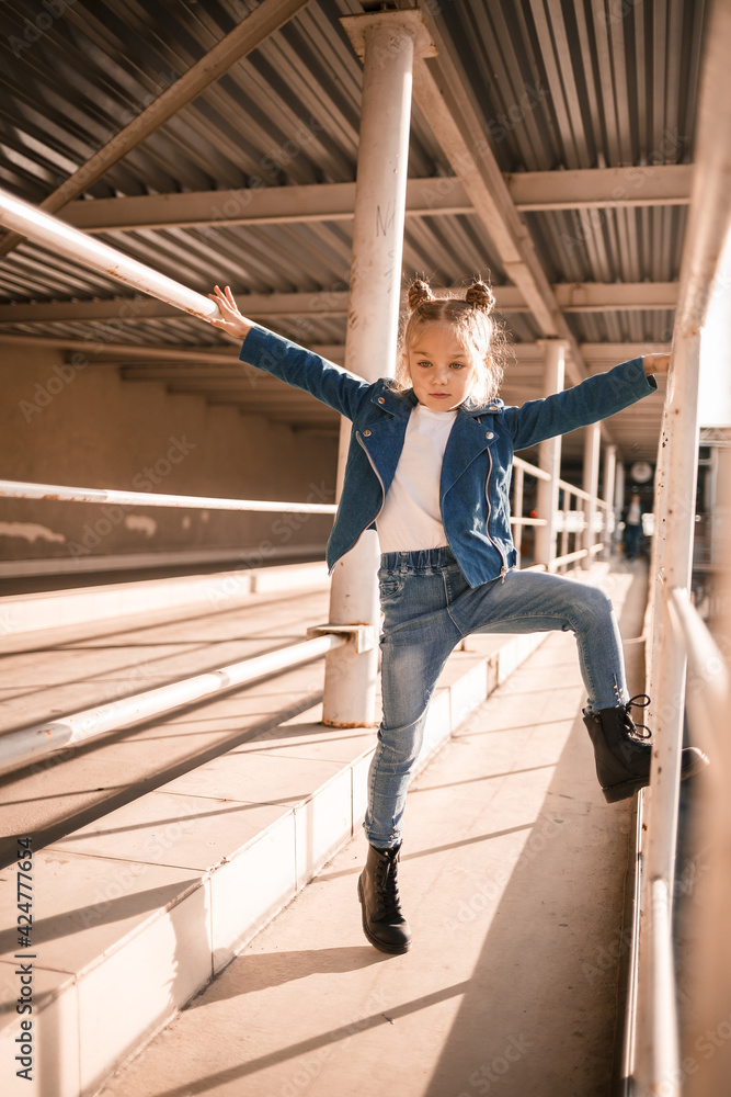 Fototapeta premium Stylish beautiful girl of about seven in a denim jacket walks on the street