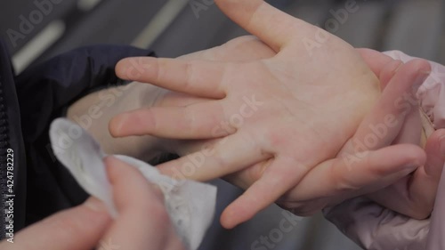Close-up of a woman cleaning dirt from a child's hands with wet antibacterial wipes