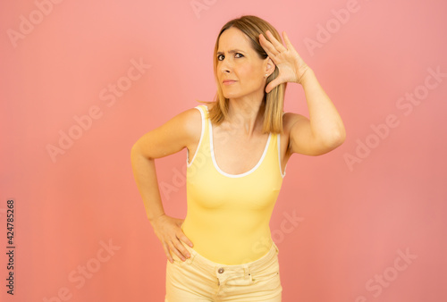 Young woman over isolated pink background listening to something by putting hand on the ear