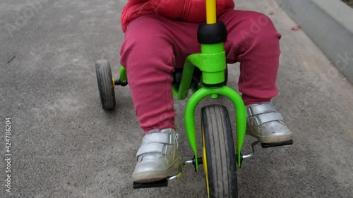 Close-up of toddler girl who rides a tricycle down the street.