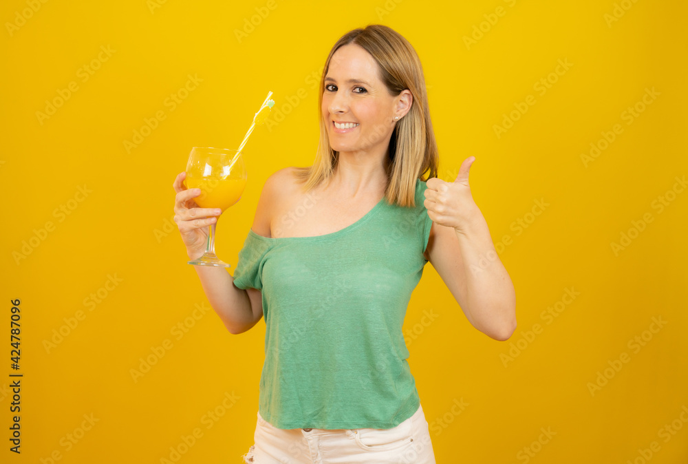 Picture of smiling young woman in casual clothes with thumb up isolated over yellow background holding cocktail. Picture of smiling young woman in casual clothes with thumb up isolated over yellow background holding cocktail.