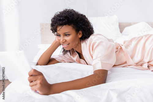 Smiling african american woman using digital tablet on blurred foreground on bed