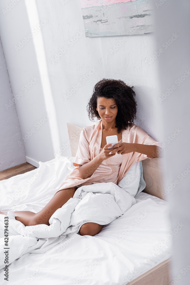 Smiling african american woman using cellphone on bed Smiling african american woman using cellphone on bed