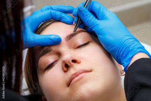 The master plucks out the excess hairs on the eyebrows with tweezers  giving them a shape.