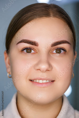A close-up of the face of a young woman who has just had a permanent eyebrow tattoo done.