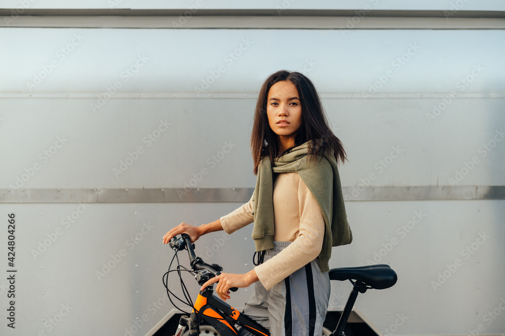 Portrait of a young attractive hispanic female biker posing for the camera, holding her orange bicycle, wearing a stylish outfit. Portrait of a young attractive hispanic female biker posing for the camera, holding her orange bicycle, wearing a stylish outfit.