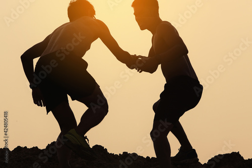Fotografia A silhouette of a men trail runner helping his teammates to cross obstacles