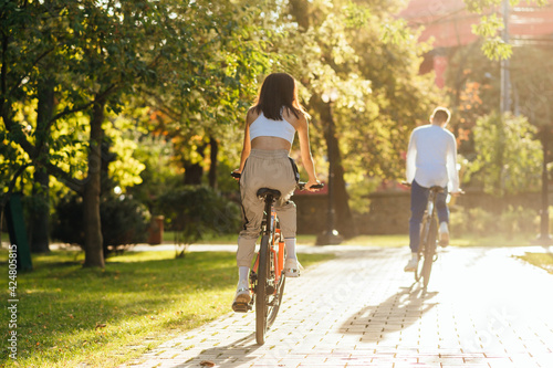 Wallpaper Mural Back view of a female rider on a bright orange bike following her boyfriend bicyclist in a modern city park on a bright summer sunny day. Torontodigital.ca