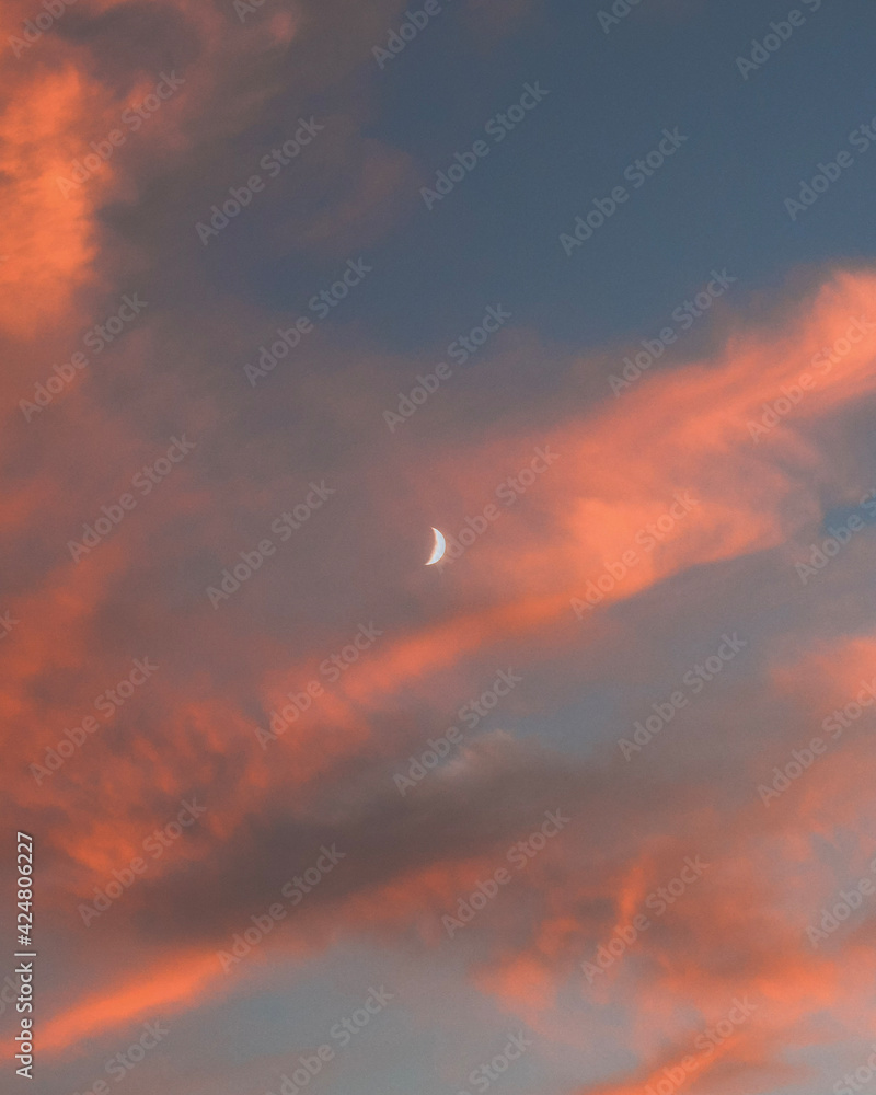 sunset in the sky with the clouds and moon lit up by the sun.