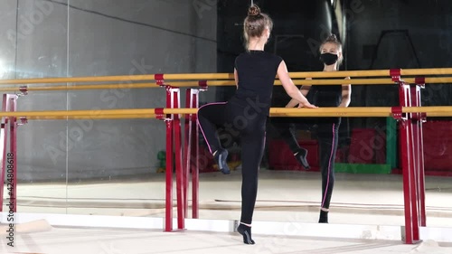 graceful girls teenager doing various art exercises and poses in medical protection face mask, stretch near ballet barre, dancer practicing with mirrors. Professional sport and preparing for competiti photo