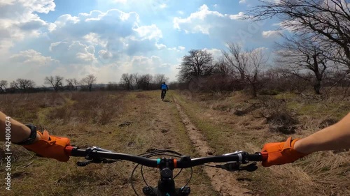 Two cyclists are riding the trail across the field. From the first person.