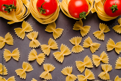 Fettuccine tagliatelle pasta and tomatoes on a gray background. Spaghetti nests. A raw ingredient for traditional Italian cuisine.  Fresh homemade meals or convenience foods. Selective focus.