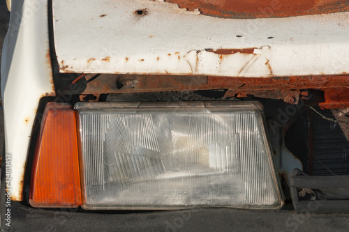 The headlight of an old wrecked rusty car.