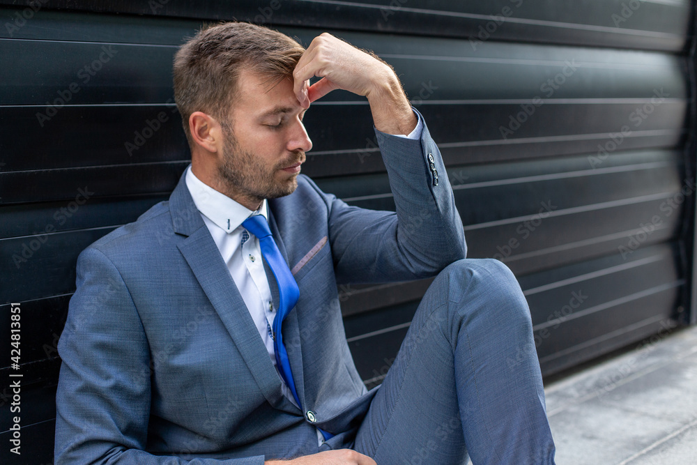 Portrait of a young tired businessman sitting on the floor in front of the building. Portrait of a young tired businessman sitting on the floor in front of the building.