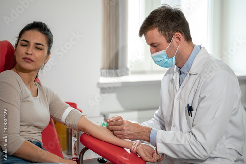 Male nurse takes blood sampling introducing a needle into a vein of woman's arm. The patient is afraid. 