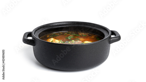 Soup with meatballsi n a black pot isolated on a white background.