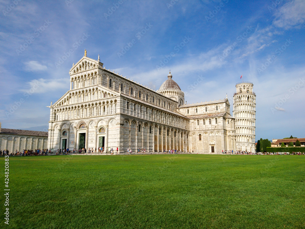 Leaning Tower of Pisa (elaborately adorned 14th-century tower) and Cattedrale di Pisa (marble-striped cathedral) on summer green grass and blue sky. Travel Italy, famous places