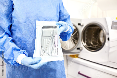 Sterilizing medical instruments in autoclave. Dental office. Nurse holding sterile medical instruments