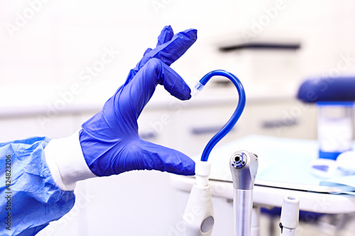 Saliva ejector and a hand in a disposable glove symbolize love in dentistry. Blue saliva ejector.The atmosphere of the dental office.With love in dentistry.Heart symbol. Selective focus 
