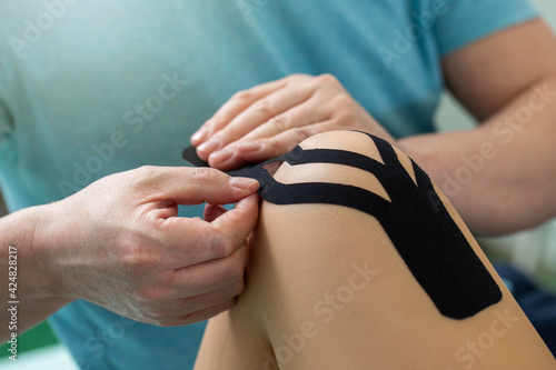 Physiotherapist applying kinesiology tape to patient knee. photo