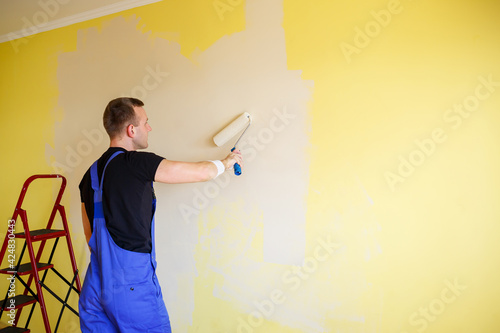 Young man in overalls hold a paint roller. Tools accessories for apartment room renovation. Home renovation concept