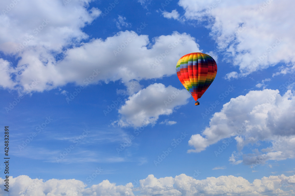 A motley multicolored hot air balloon raises a basket with tourists in the blue sky among white clouds. A motley multicolored hot air balloon raises a basket with tourists in the blue sky among white clouds.