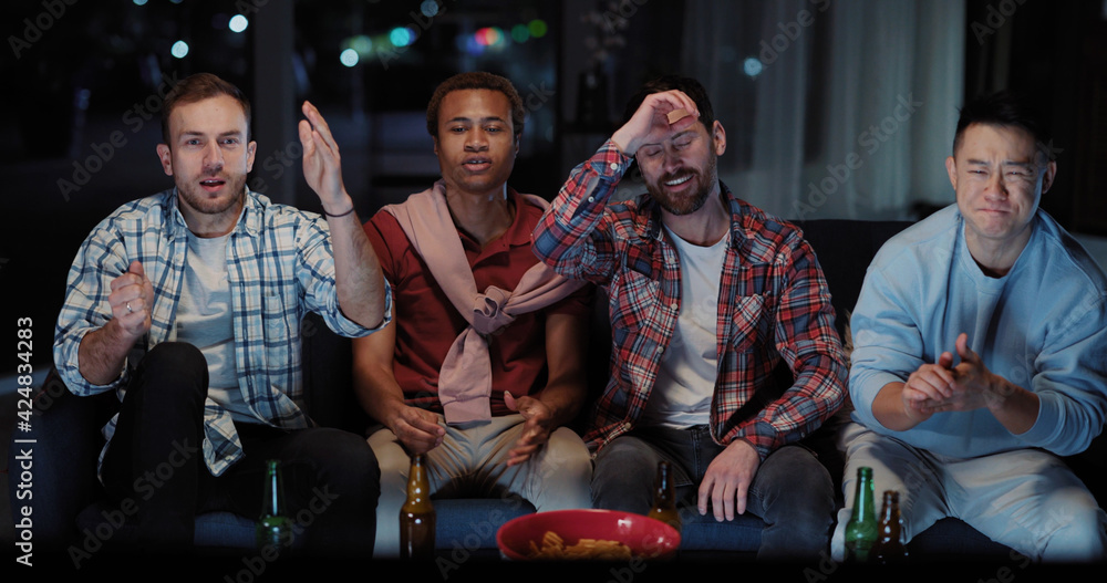 Young attractive diverse men watching TV football game competition match together and communicating at night. Nightlife activity. Male friendship.