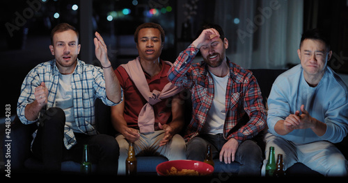 Young attractive diverse men watching TV football game competition match together and communicating at night. Nightlife activity. Male friendship.