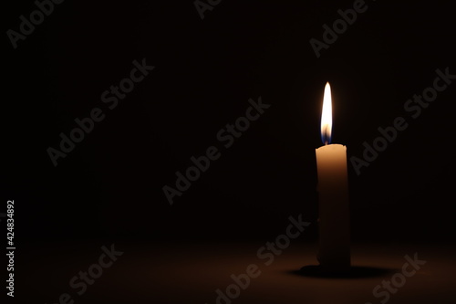 A candle burning alone in a dark room. 