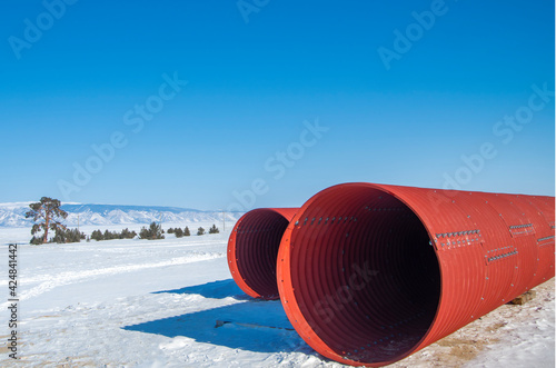 Pipeline, red metal pipes in winter lie on the snow against the background of a cloudless blue sky