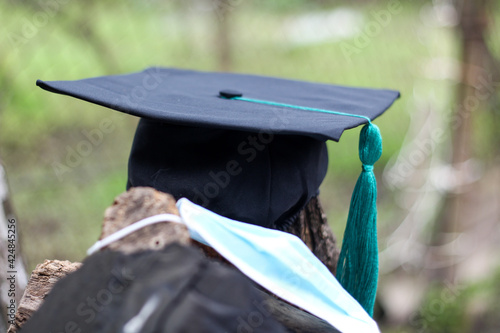 Black graduation cap with blue tassel with medical mask in the natural environment. Horizontal image