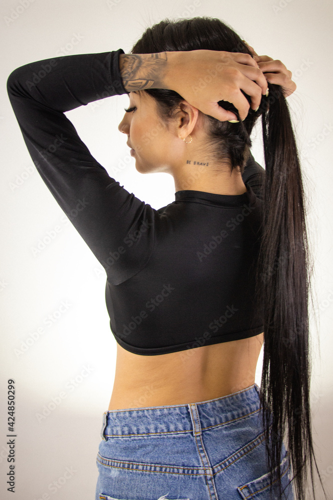 Foto de Mujer joven morena sexy vistiendo ropa juvenil de color negro,  hermosa chica con cabello negro largo y morena vistiendo blusa corta de  color negro do Stock