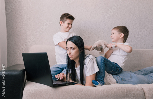 noisy children distract mothers from working at the computer. annoyed mom holds her head