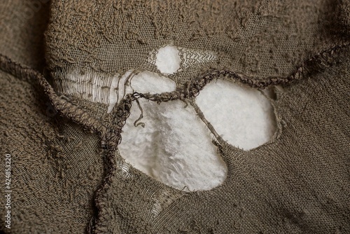 a piece of old clothing made of torn gray green fabric with a seam and a large white hole