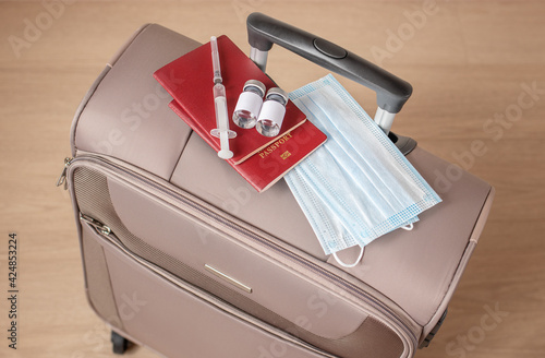 Top view of an suitcase with a covid-19 vaccine and a syringe, passport and medical masks. Concept: coronavirus vaccination and travel