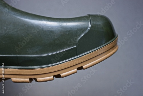 part of a green rubber boot with a brown sole on a gray background © butus