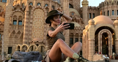 beautiful woman sits on the grass, after hiking, in desert boots, makes a selfie on a mobile phone against the background of a mosque.tourist with a backpack takes pictures of herself photo