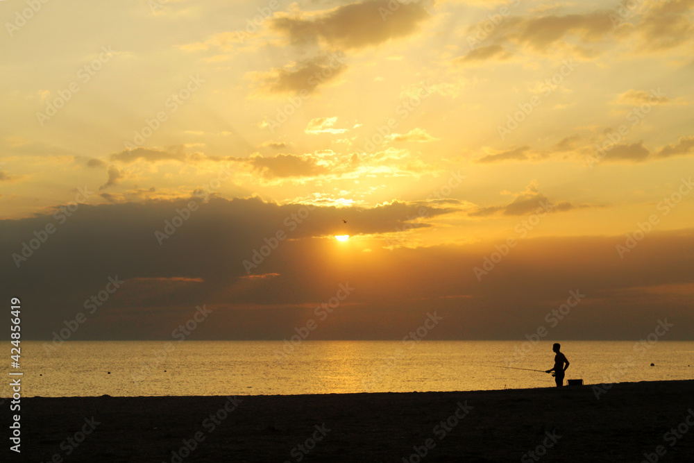 Silhouette of a fisherman at sunset by the sea. Sea fishing. Fishing from the shore.