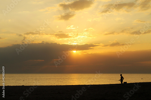 Silhouette of a fisherman at sunset by the sea. Sea fishing. Fishing from the shore.