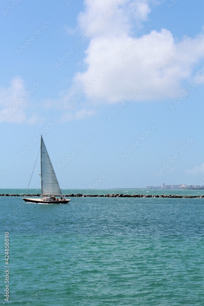 Obraz premium Sailboat sailing at low tide with passengers aboard navigating through the wind in Miami Beach, Florida near South Pointe Pier. Copyspace for text. Advertising. 