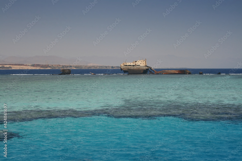 The sunken shipwreck on the reef, Tiran island, Egypt, Red Sea. Old rusty wreckage of a cargo ship on the turquoise sea surface. The sunken shipwreck on the reef, Tiran island, Egypt, Red Sea. Old rusty wreckage of a cargo ship on the turquoise sea surface.