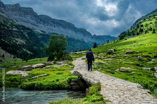 Un hombre de espaldas camina por el circo glaciar del Parque Nacional de Ordesa, España, con el fondo de los bosques y montañas del Pirineo español