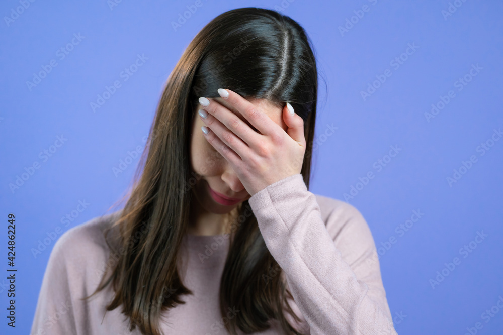 Portrait of young woman doing facepalm gesture, like no, I forgot. Unhappy woman with long hair feeling sorrow, regret, drama, failure. She isolated on violet wall
