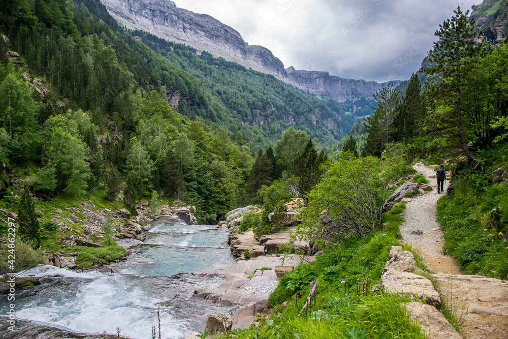 Un senderista pasea por un camino junto al río Arazas descendiendo hacia el bosque mixto de coníferas y hayas del Parque Nacional de Ordesa, en los Pirineos españoles Un senderista pasea por un camino junto al río Arazas descendiendo hacia el bosque mixto de coníferas y hayas del Parque Nacional de Ordesa, en los Pirineos españoles