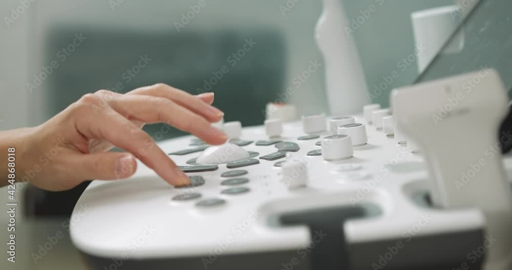 Close up cropped shot of modern medical device, ultrasound machine scanner at work. Hand of professional female doctor sonographer pushing buttons on ultrasound control panel Close up cropped shot of modern medical device, ultrasound machine scanner at work. Hand of professional female doctor sonographer pushing buttons on ultrasound control panel