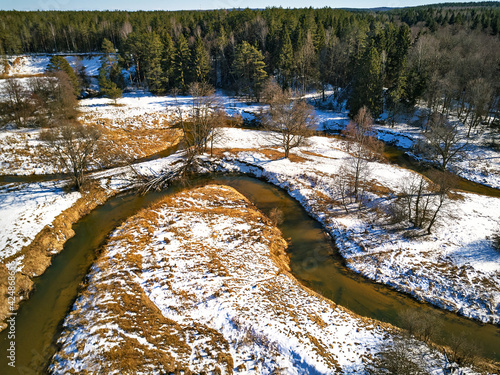 Obraz na płótnie Early spring landscape with melting snow and thawed patches in meadow. Forest and Isloch creek in sunny march day. w salonie
