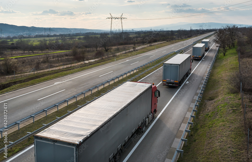 Φωτογραφία Convoy of Big Transportation trucks departing on a country highway under a sunset sky