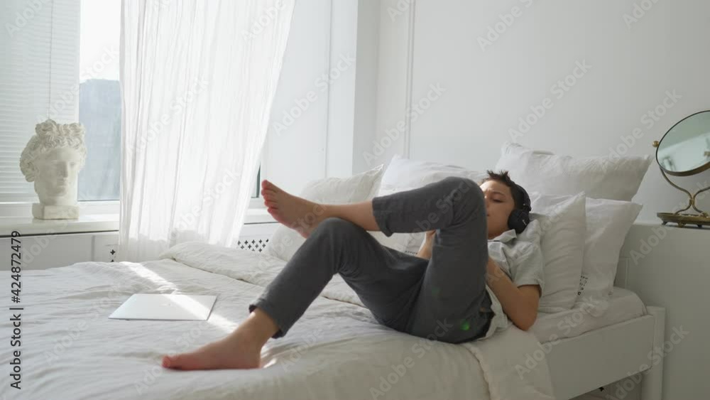 11 years old boy lies on the bed and listens to music with headphones. High quality 4k footage 11 years old boy lies on the bed and listens to music with headphones. High quality 4k footage